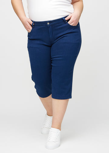 Mörkblå regular capris, modellnamn Royals, som sitter rakt längs benet och slutar strax under knät på en plus size-modell, sedd framifrån.