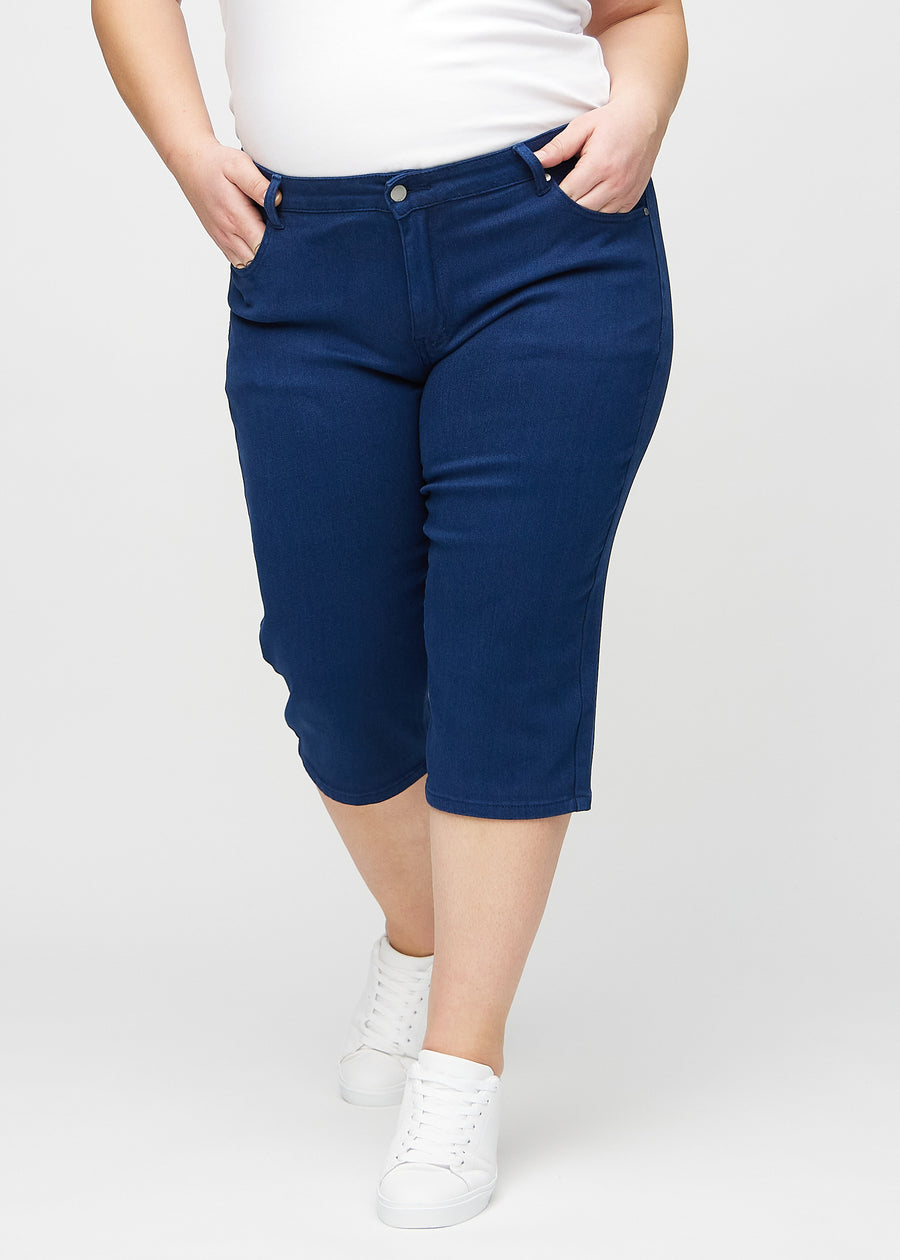 Mörkblå regular capris, modellnamn Royals, som sitter rakt längs benet och slutar strax under knät på en plus size-modell, sedd framifrån.