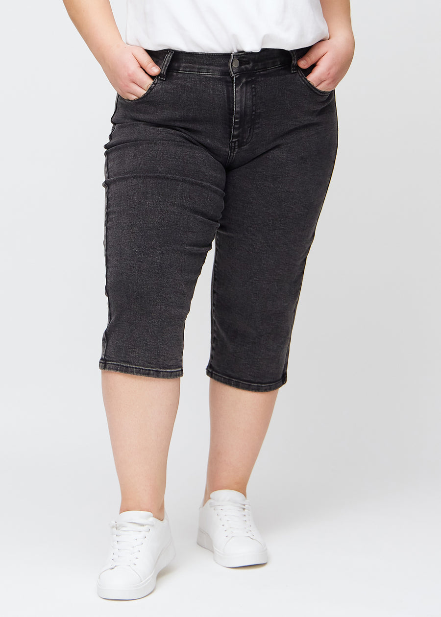 Mörkgrå denim regular capris, modellnamn Shadows, som sitter rakt längs benet och slutar precis under knät på en plus-size-modell, sedd framifrån.