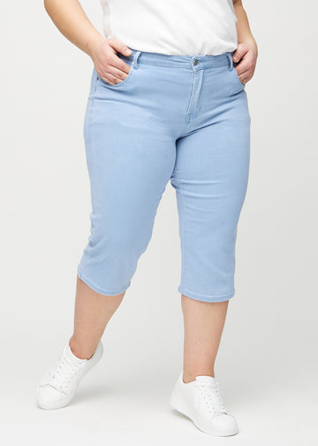 Ljusblå regular capris, modellnamn Skies, som sitter rakt längs benet och slutar precis under knät på en plus size-modell, sedd framifrån.
