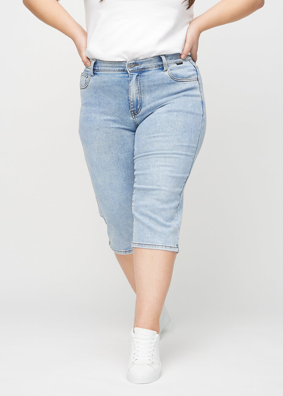 Ljus denim regular capris, modellnamn Waves, som sitter rakt längs benet och slutar precis under knät på en plus-size-modell, sedd framifrån.