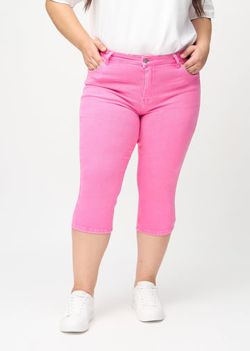 Skinnycapris för kvinnor i pastellrosa jeanstyg, färgen Flamingos. Framifrån på en plus size-modell, med åtsittande ben till strax under knät.
