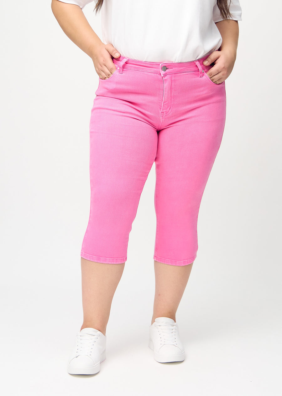Skinnycapris för kvinnor i pastellrosa jeanstyg, färgen Flamingos. Framifrån på en plus size-modell, med åtsittande ben till strax under knät.