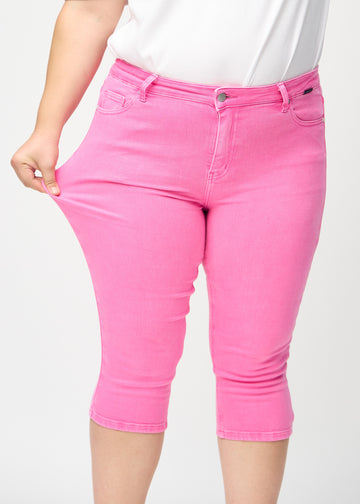 Skinnycapris för kvinnor i pastellrosa jeanstyg, färgen Flamingos. En plus size-modell drar i tyget för att visa flexibiliteten.