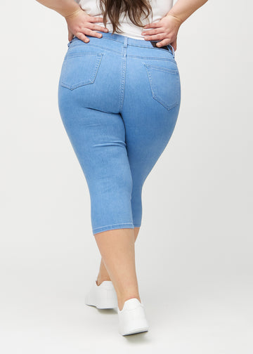 Skinnycapris för kvinnor i blått jeanstyg, färgen Geraniums. Bakifrån på en plus size-modell, med fokus på passform och bakfickor.
