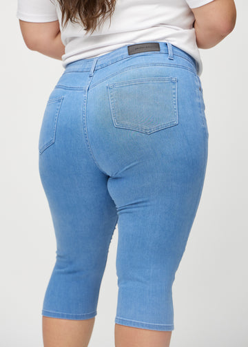 Skinnycapris för kvinnor i blått jeanstyg, färgen Geraniums. Närbild bakifrån på en plus size-modell, med fokus på fickor och sömmar.