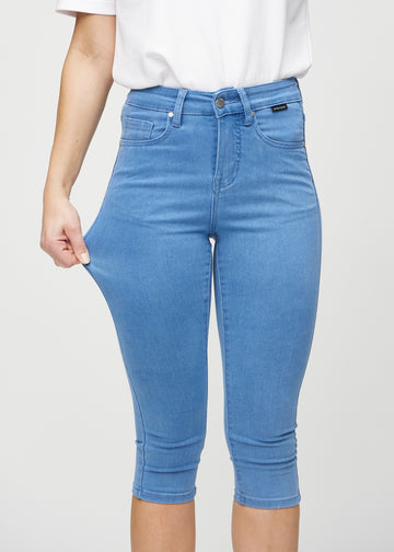 Skinnycapris för kvinnor i blått jeanstyg, färgen Geraniums. En modell drar i tyget för att visa flexibiliteten.