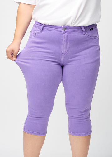 Skinnycapris för kvinnor i pastellila jeanstyg, färgen Lavenders. En plus size-modell drar i tyget för att visa flexibiliteten.