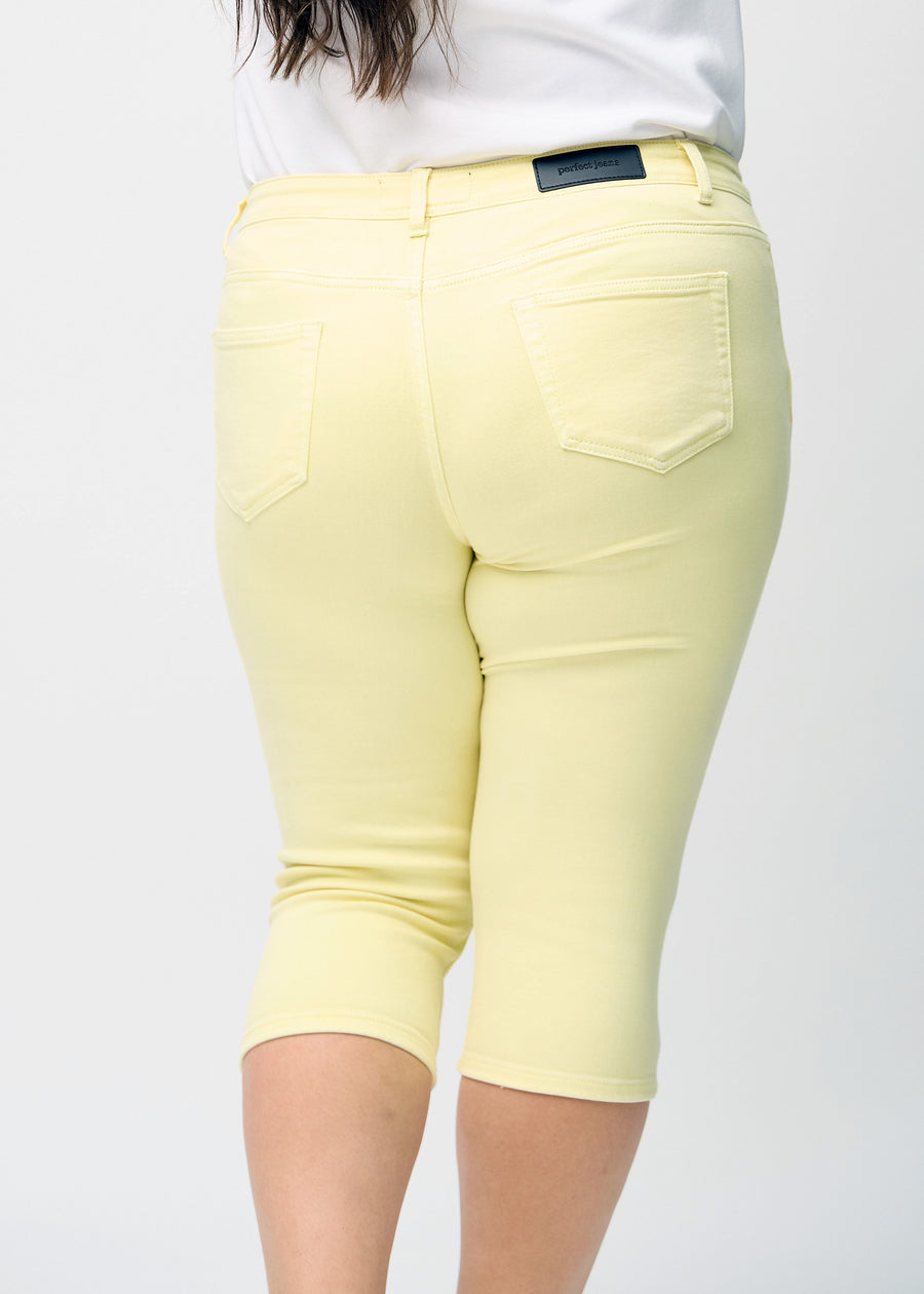 Skinnycapris för kvinnor i pastellgult jeanstyg, färgen Lemonades. Närbild bakifrån på en plus size-modell, med fokus på fickor och sömmar.