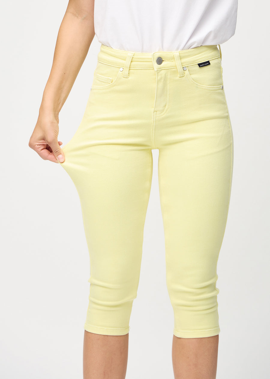 Skinnycapris för kvinnor i pastellgult jeanstyg, färgen Lemonades. En modell drar i tyget för att visa flexibiliteten.