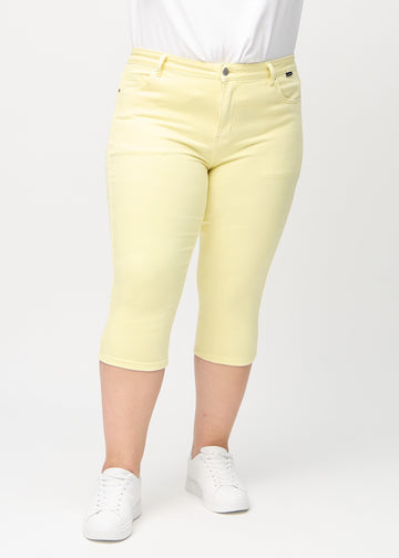 Skinnycapris för kvinnor i pastellgult jeanstyg, färgen Lemonades. Framifrån på en plus size-modell, med åtsittande ben till strax under knät.