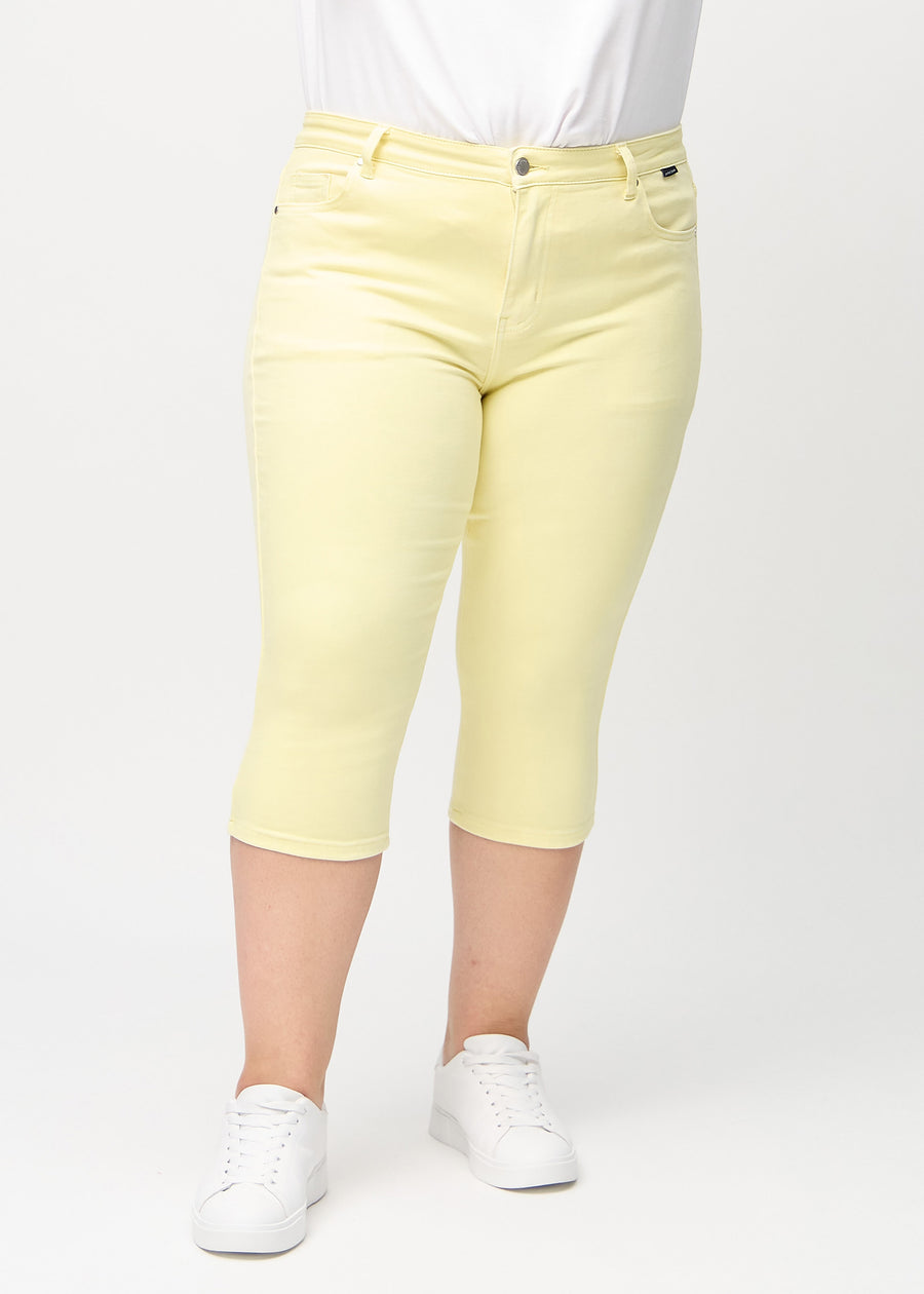 Skinnycapris för kvinnor i pastellgult jeanstyg, färgen Lemonades. Framifrån på en plus size-modell, med åtsittande ben till strax under knät.