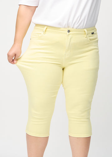 Skinnycapris för kvinnor i pastellgult jeanstyg, färgen Lemonades. En plus size-modell drar i tyget för att visa flexibiliteten.