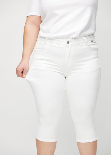 Skinnycapris för kvinnor i vitt jeanstyg, färgen Marguerites. En plus size-modell drar i tyget för att visa flexibiliteten.
