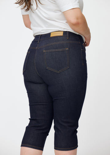 Mörkblå denim capris för dam i färgen Midnights sett bakifrån i närbild på plus-size modell.