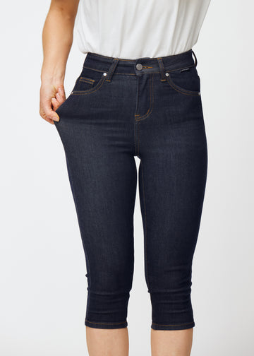 Modell sträcker mörkblå denim capris för dam i färgen Midnights vid låret för att visa materialets stretch.