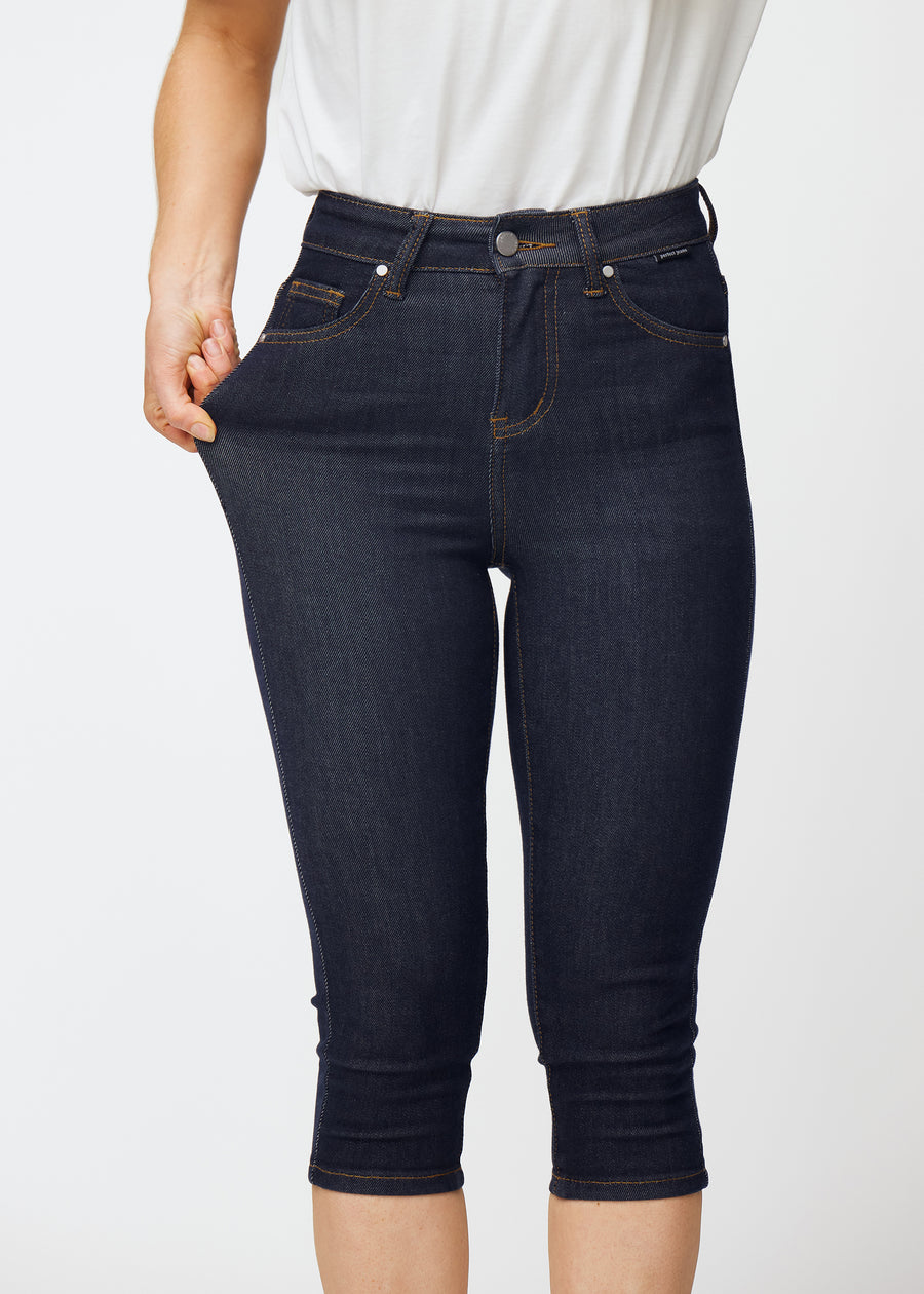 Modell sträcker mörkblå denim capris för dam i färgen Midnights vid låret för att visa materialets stretch.