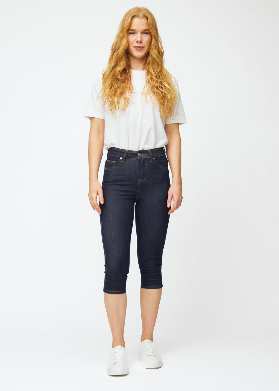 Helbild av modell i mörkblå denim capris för dam i färgen Midnights med skinny passform.