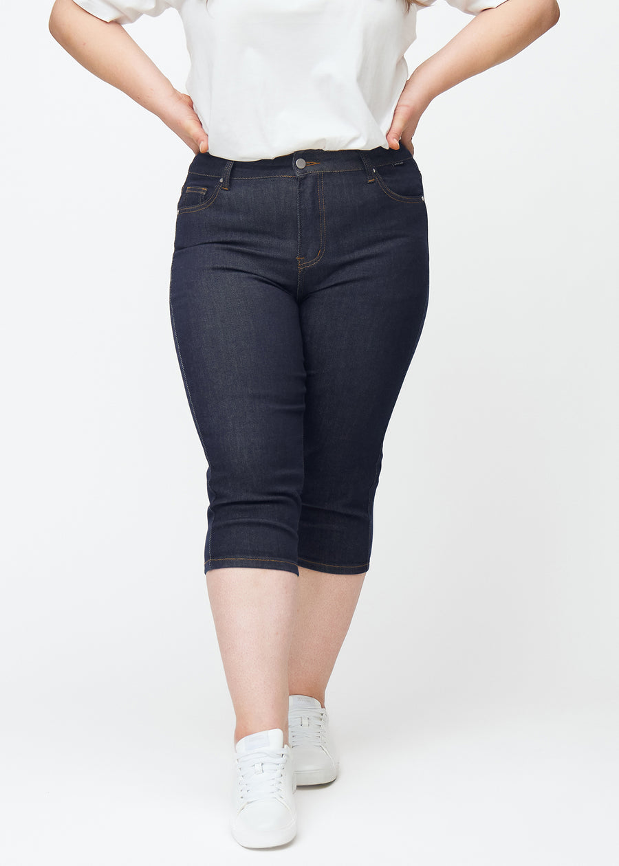 Mörkblå denim capris för dam i färgen Midnights med skinny passform sett framifrån på plus-size modell.