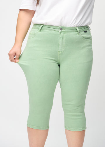 Skinnycapris för kvinnor i pastellgrönt jeanstyg, färgen Mints. En plus size-modell drar i tyget för att visa flexibiliteten.