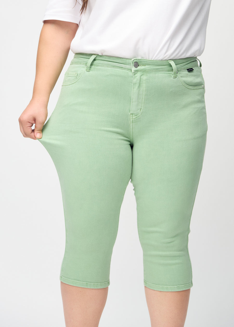 Skinnycapris för kvinnor i pastellgrönt jeanstyg, färgen Mints. En plus size-modell drar i tyget för att visa flexibiliteten.
