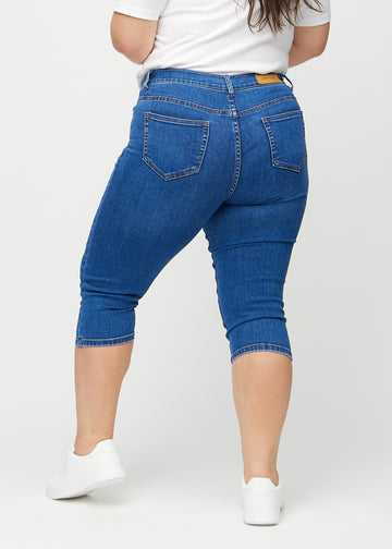 Skinnycapris för kvinnor i mörkblå denim, färgen Oceans. Bakifrån på en plus size-modell, med fokus på passform och bakfickor.