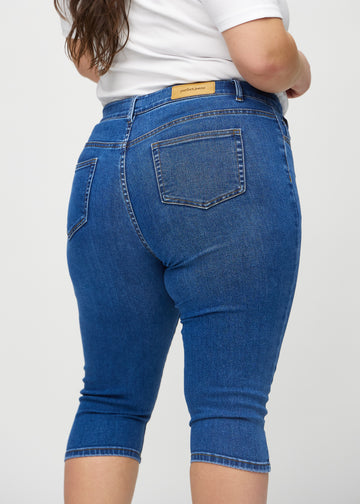 Skinnycapris för kvinnor i mörkblå denim, färgen Oceans. Närbild bakifrån på en plus size-modell, med fokus på fickor och sömmar.