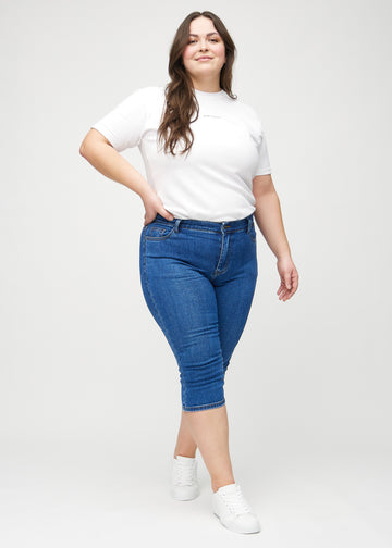 Skinnycapris för kvinnor i mörkblå denim, färgen Oceans. Helbild av en plus size-modell som bär capris.