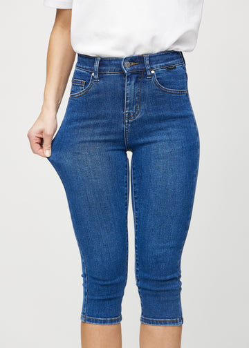 Skinnycapris för kvinnor i mörkblå denim, färgen Oceans. En modell drar i tyget för att visa flexibiliteten.