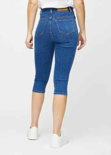 Skinnycapris för kvinnor i mörkblå denim, färgen Oceans. Bakifrån på en modell, med fokus på passform och bakfickor.
