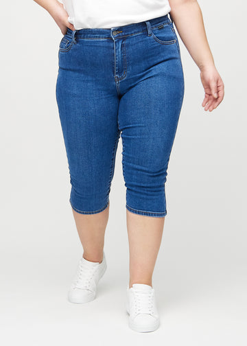 Skinnycapris för kvinnor i mörkblå denim, färgen Oceans. Framifrån på en plus size-modell, med åtsittande ben till strax under knät.