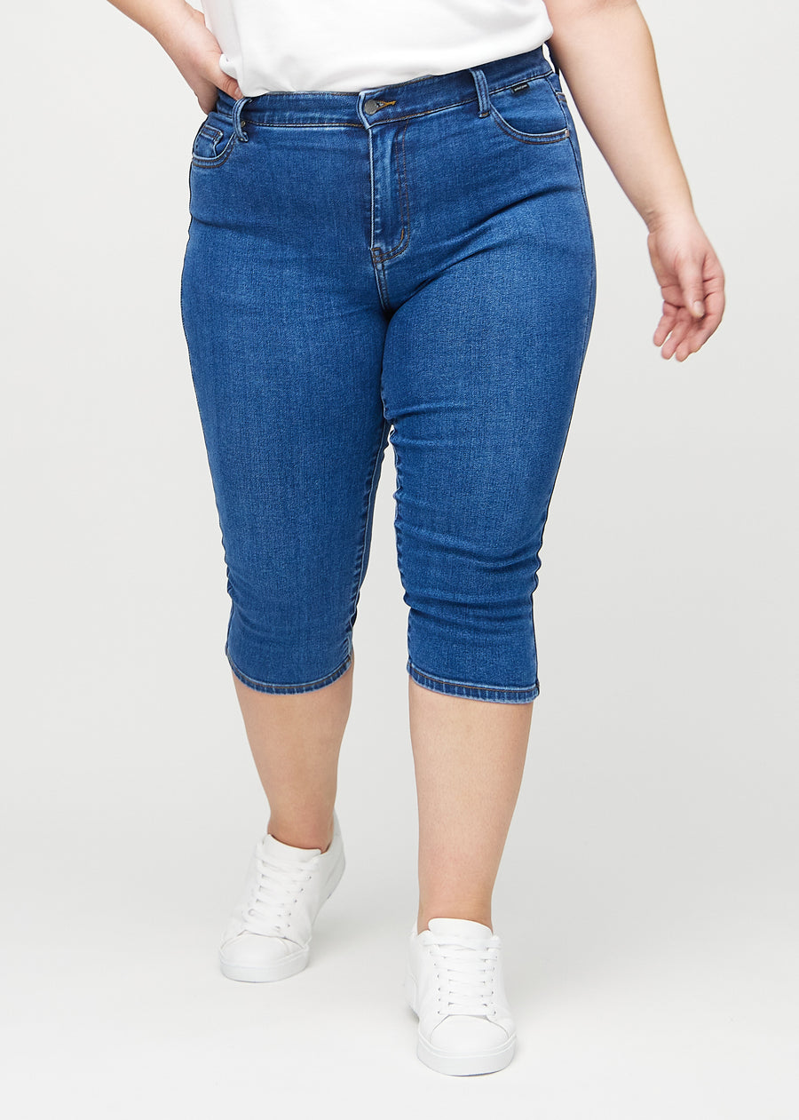 Skinnycapris för kvinnor i mörkblå denim, färgen Oceans. Framifrån på en plus size-modell, med åtsittande ben till strax under knät.
