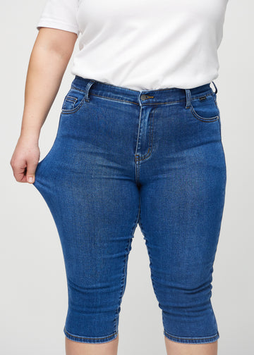 Skinnycapris för kvinnor i mörkblå denim, färgen Oceans. En plus size-modell drar i tyget för att visa flexibiliteten.