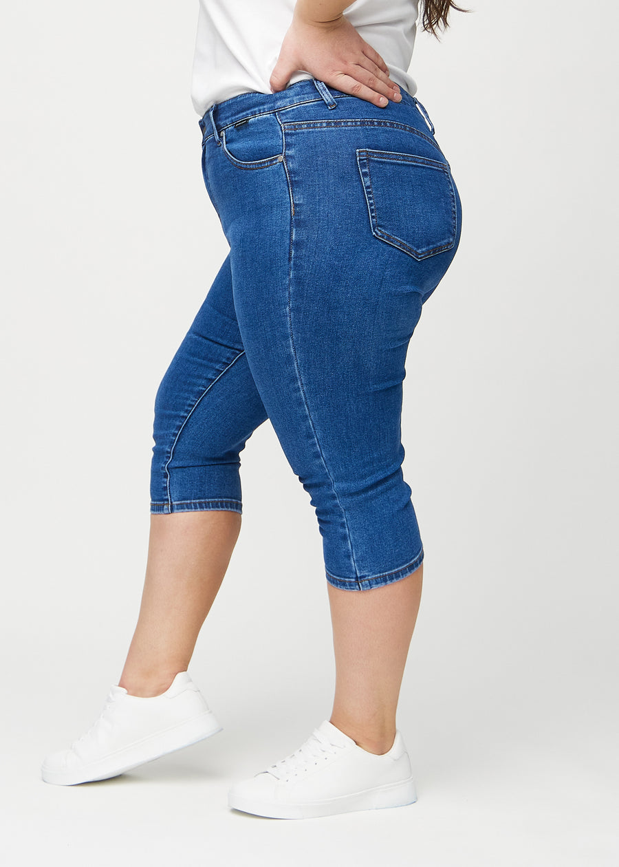 Skinnycapris för kvinnor i mörkblå denim, färgen Oceans. Från sidan på en plus size-modell, med åtsittande passform.