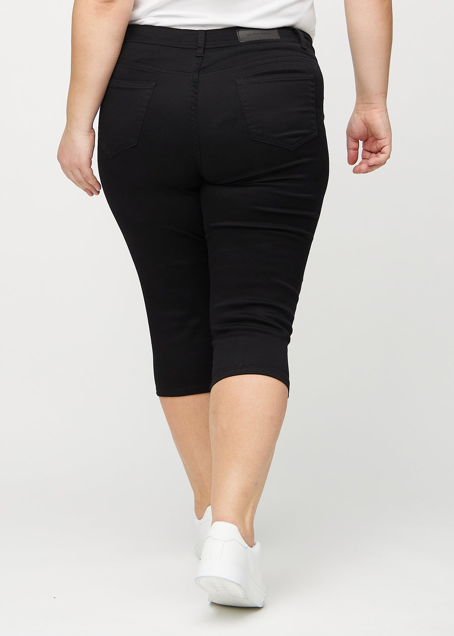 Svarta skinny capris sedda bakifrån på en plus-size-modell, så att hela produkten syns.
