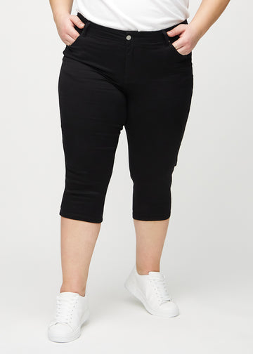 Svarta skinny capris, modellnamn Ravens, som sitter tätt längs benet och slutar precis under knät på en plus-size-modell, framifrån.