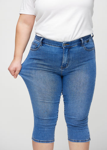 Plus size-modellen drar ut capribyxorna vid låret för att visa stretch.