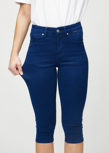 Skinnycapris för kvinnor i mörkblått jeanstyg, färgen Royals. En modell drar i tyget för att visa flexibiliteten.