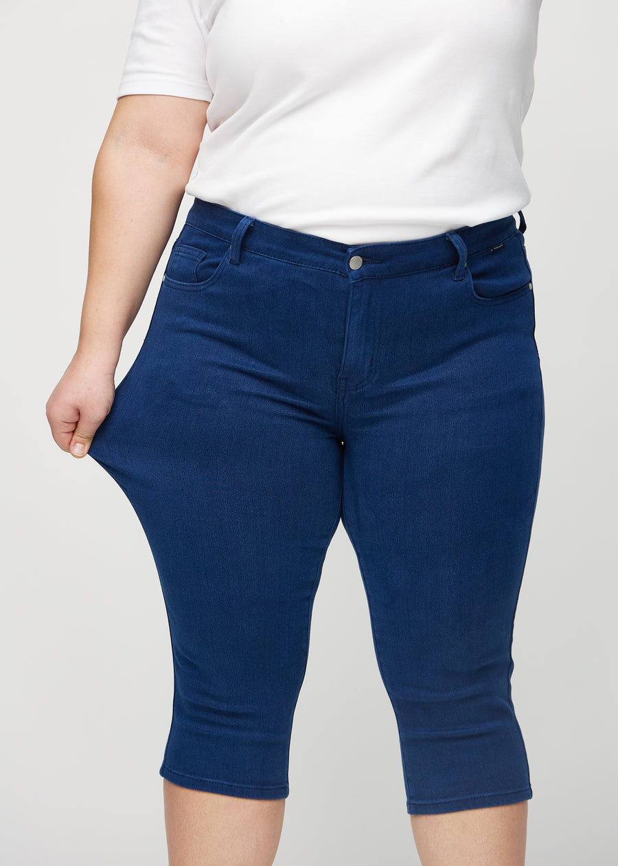 Skinnycapris för kvinnor i mörkblått jeanstyg, färgen Royals. En plus size-modell drar i tyget för att visa flexibiliteten.