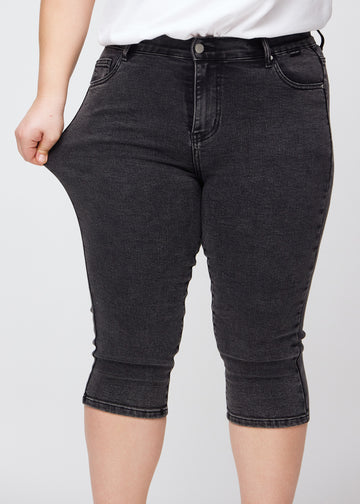 Skinnycapris för kvinnor i mörkgrå denim, färgen Shadows. En plus size-modell drar i tyget för att visa flexibiliteten.