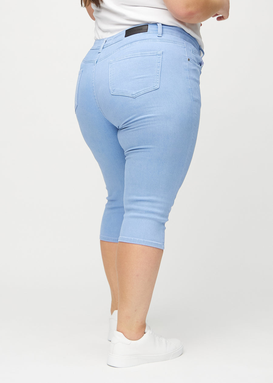 Ljusblå skinny capris sett bakifrån på en plus-size-modell, så att man kan se hela produkten.
