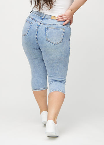 Skinnycapris för kvinnor i ljusblå denim, färgen Waves. Bakifrån på en plus size-modell, med fokus på passform och bakfickor.