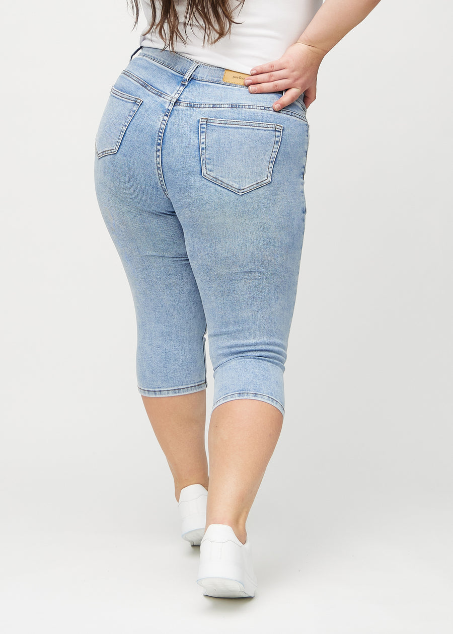 Skinnycapris för kvinnor i ljusblå denim, färgen Waves. Bakifrån på en plus size-modell, med fokus på passform och bakfickor.