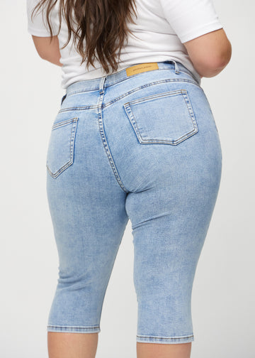 Skinnycapris för kvinnor i ljusblå denim, färgen Waves. Närbild bakifrån på en plus size-modell, med fokus på fickor och sömmar.
