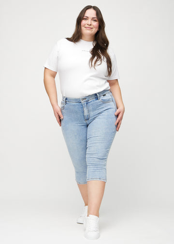 Skinnycapris för kvinnor i ljusblå denim, färgen Waves. Helbild av en plus size-modell som bär capris.