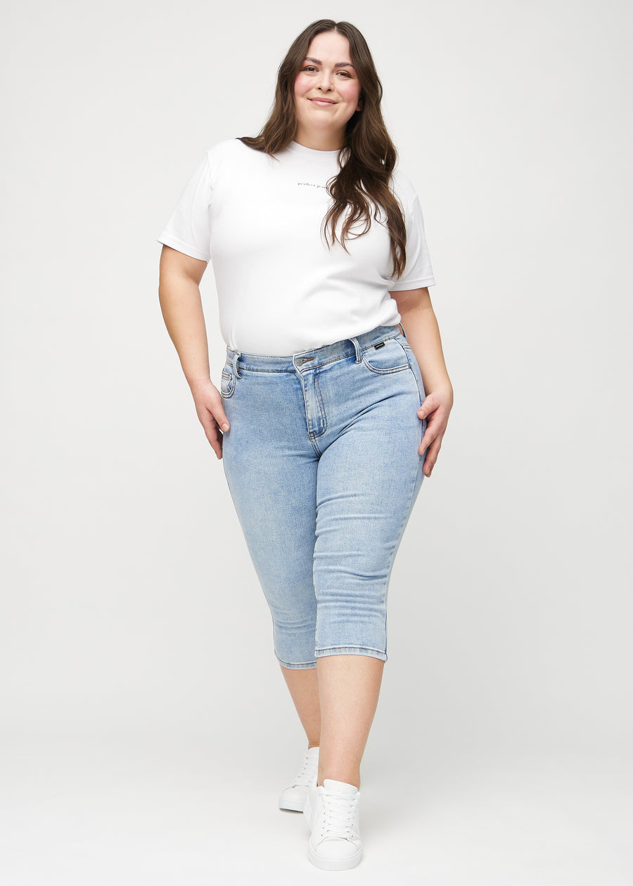 Skinnycapris för kvinnor i ljusblå denim, färgen Waves. Helbild av en plus size-modell som bär capris.
