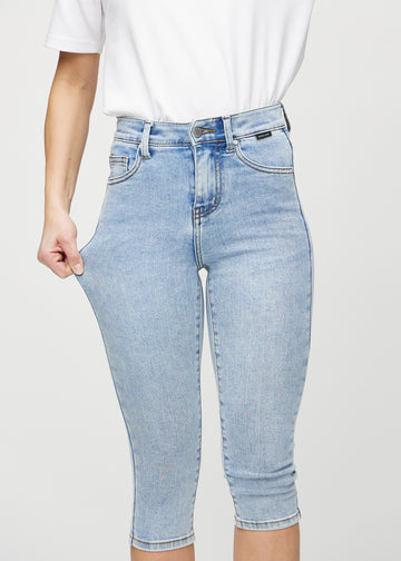 Skinnycapris för kvinnor i ljusblå denim, färgen Waves. En modell drar i tyget för att visa flexibiliteten.