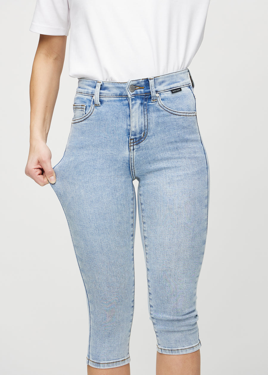 Skinnycapris för kvinnor i ljusblå denim, färgen Waves. En modell drar i tyget för att visa flexibiliteten.