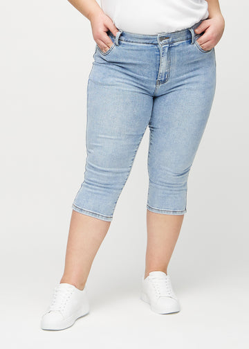 Skinnycapris för kvinnor i ljusblå denim, färgen Waves. Framifrån på en plus size-modell, med åtsittande ben till strax under knät.