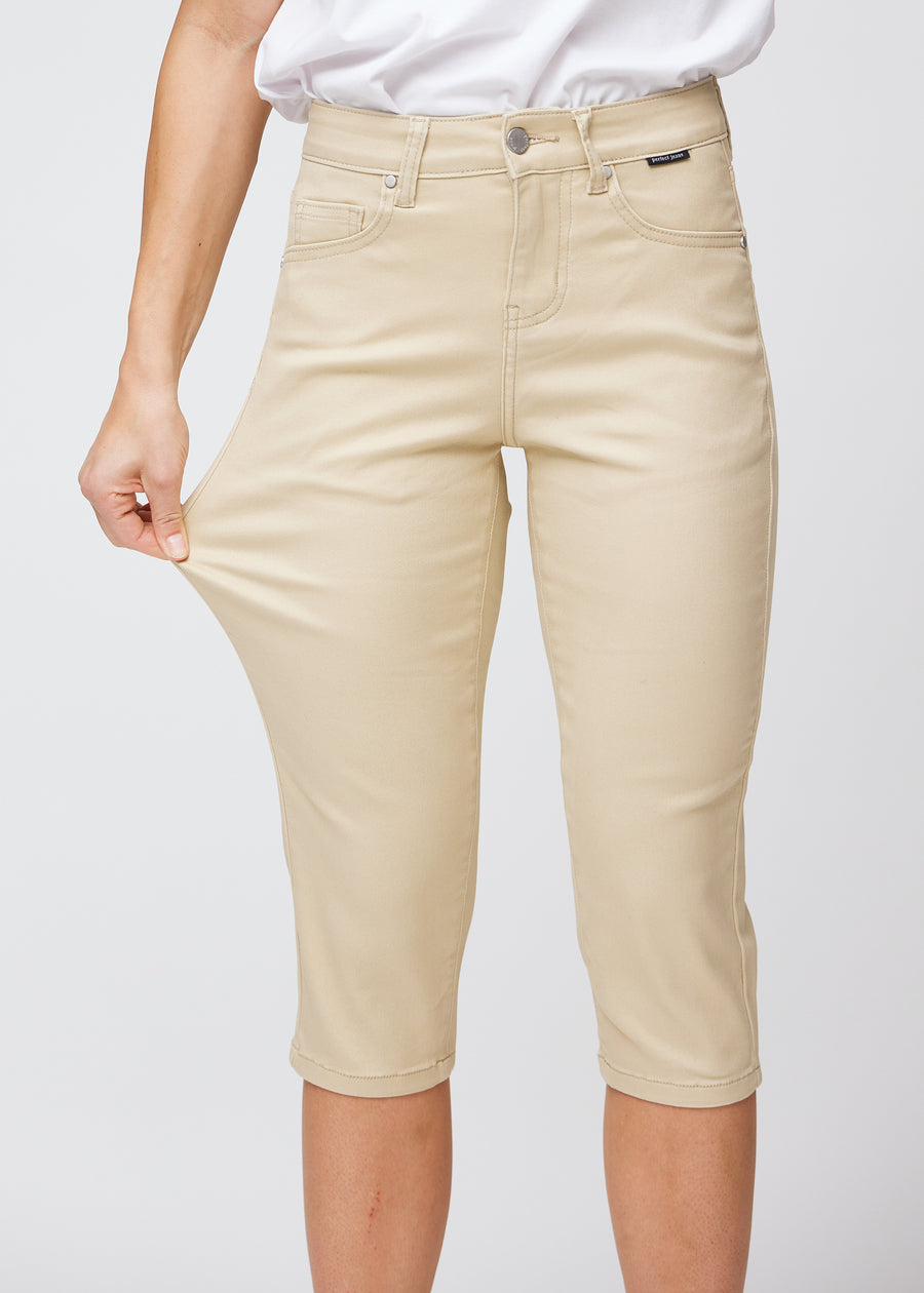 Slimcapris för kvinnor i beige jeanstyg, färgen Gazelles. En modell drar i tyget vid låret för att visa stretch och flexibilitet.